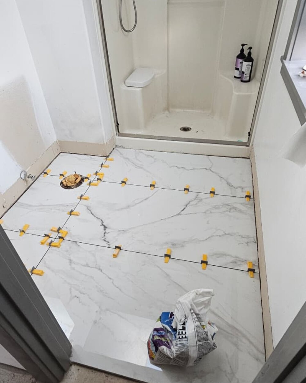 Marble-look tile floor with leveling clips in a bathroom